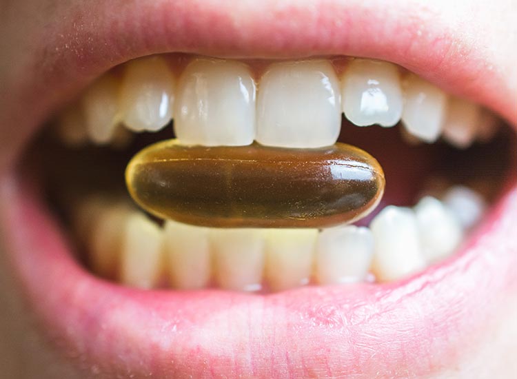 Close-up of a person holding a softgel vitamin capsule between their teeth